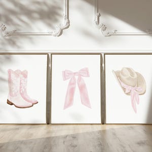 K&ouml;nnte beinhalten: Drei gerahmte Kunstdrucke mit Aquarellillustrationen. Die Drucke zeigen ein Paar rosa Cowboystiefel, eine rosa Schleife und einen Cowboyhut mit einer rosa Schleife. Das Kunstwerk ist vor einem wei&szlig;en Hintergrund.