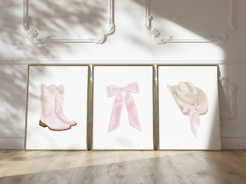 K&ouml;nnte beinhalten: Drei gerahmte Kunstdrucke mit Aquarellillustrationen. Die Drucke zeigen ein Paar rosa Cowboystiefel, eine rosa Schleife und einen Cowboyhut mit einer rosa Schleife. Das Kunstwerk ist vor einem wei&szlig;en Hintergrund.