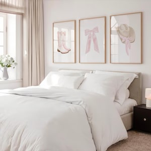 K&ouml;nnte beinhalten: Drei gerahmte Kunstdrucke &uuml;ber einem Bett. Die Drucke zeigen einen rosa Cowboy-Stiefel, eine rosa Schleife und einen Cowboyhut mit einer rosa Schleife. Das Bett hat wei&szlig;e Bettw&auml;sche und Kissen. Ein Nachttisch und eine Lampe befinden sich rechts.
