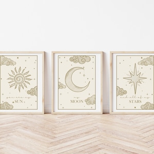 May include: Three framed art prints with celestial designs. The prints feature a sun, moon, and star, each surrounded by clouds and text. The frames are light-colored, and the artwork has a neutral color palette.