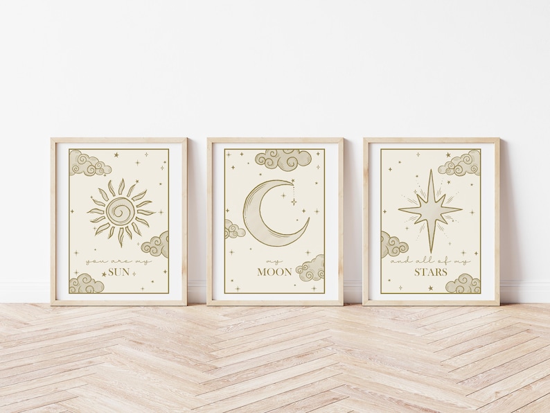 May include: Three framed art prints with celestial designs. The prints feature a sun, moon, and star, each surrounded by clouds and text. The frames are light-colored, and the artwork has a neutral color palette.