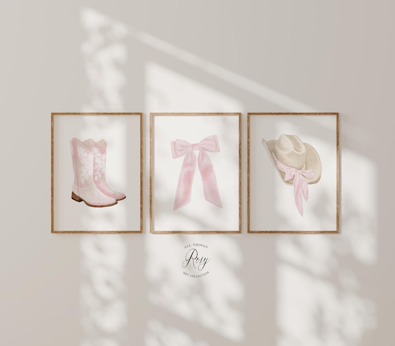 K&ouml;nnte beinhalten: Drei gerahmte Aquarelldrucke. Einer zeigt rosa Cowboystiefel, ein weiterer eine rosa Schleife und der dritte einen beigefarbenen Cowboyhut mit einer rosa Schleife. Die Drucke sind in Holzrahmen auf einer neutralen Wand. Text: "All Things Rosy Art Collection".