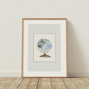 K&ouml;nnte beinhalten: Ein gerahmter Druck mit einer Aquarellillustration eines Globus. Der Globus ist in Blau- und Gr&uuml;nt&ouml;nen gehalten und vor einem cremefarbenen Hintergrund mit einem hellblauen Rand platziert. Der Rahmen ist aus Naturholz, und der Hintergrund hat vertikale Streifen.