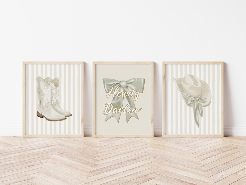 May include: Three framed prints with a western theme. The prints feature watercolor illustrations of cowboy boots, a bow with the text "Howdy Darlin'," and a cowboy hat. The backgrounds have a striped pattern in neutral tones.