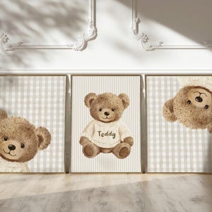 May include: Three framed prints with watercolour illustrations of teddy bears. One bear wears a sweater with the word "Teddy". The backgrounds have checkered and striped patterns in neutral tones. The prints are on a light wood floor.