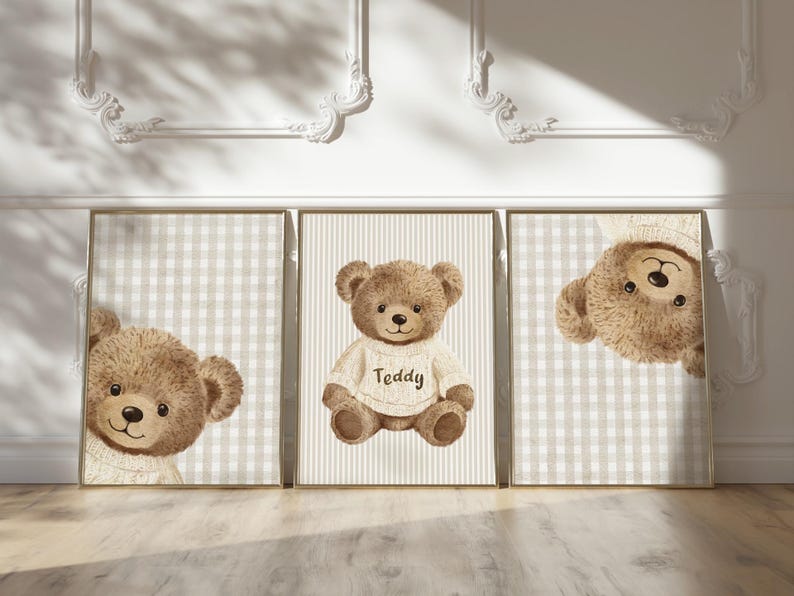 May include: Three framed prints with watercolour illustrations of teddy bears. One bear wears a sweater with the word "Teddy". The backgrounds have checkered and striped patterns in neutral tones. The prints are on a light wood floor.