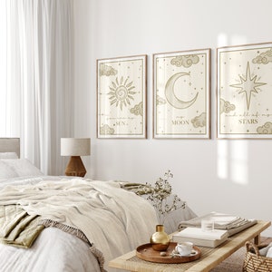 May include: Three framed art prints with celestial designs. The prints feature a sun, moon, and star, each with accompanying text. The artwork is in a neutral color palette with a light wood frame, suitable for bedroom decor.
