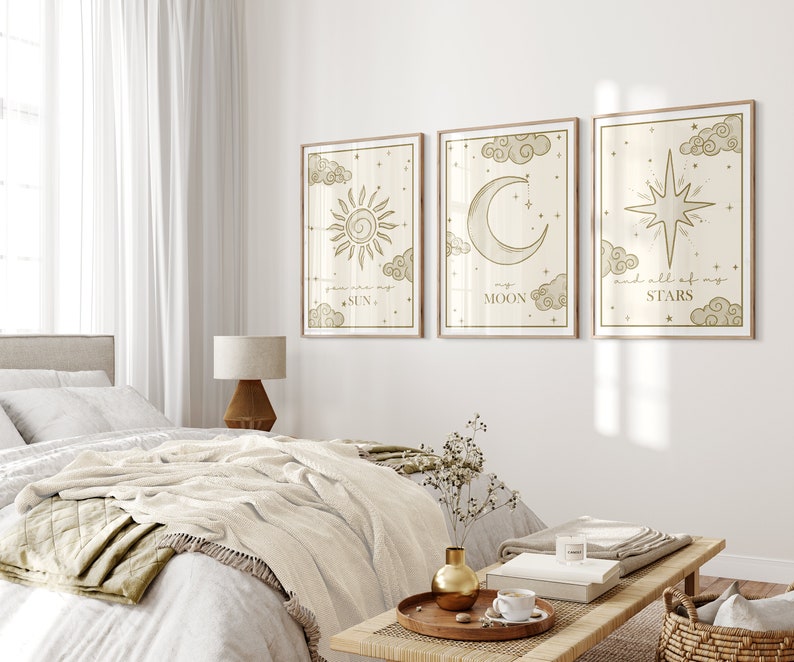 May include: Three framed art prints with celestial designs. The prints feature a sun, moon, and star, each with accompanying text. The artwork is in a neutral color palette with a light wood frame, suitable for bedroom decor.