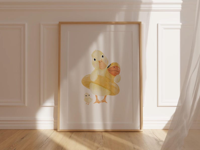 May include: Watercolor illustration of a mother duck and two ducklings. The mother duck is yellow with an orange beak and is holding a yellow floatie. The ducklings are yellow with orange beaks. The artwork is framed in a light wood frame.