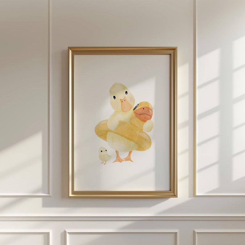 May include: A framed watercolor print featuring a yellow duckling wearing a yellow inflatable ring, with a smaller duckling standing nearby. The artwork has a gold frame and is set against a white background.