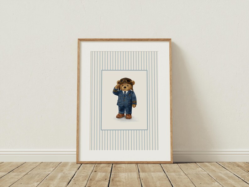 K&ouml;nnte beinhalten: Gerahmter Kunstdruck mit einem braunen Teddyb&auml;ren in einem blauen Fliegeranzug, braunen Stiefeln und einer Leder-Fliegerm&uuml;tze. Das Kunstwerk ist vor einem hellen Hintergrund mit vertikalen Streifen in einem Holzrahmen gerahmt.