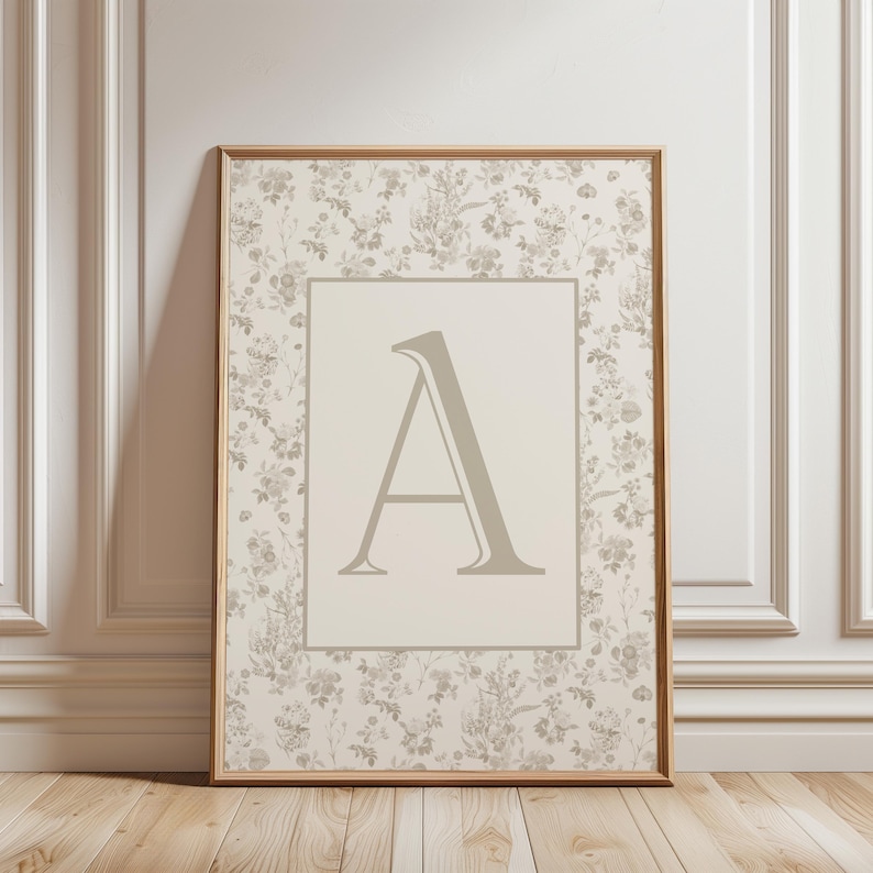 Pu&ograve; includere: Stampa incorniciata con la lettera "A". L'opera presenta uno sfondo floreale nei toni del crema e del grigio, con una cornice in legno. La lettera "A" &egrave; di colore grigio chiaro ed &egrave; centrata all'interno di un rettangolo color crema.