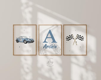 May include: Three framed prints with a racing theme. One features a light blue race car, another a blue letter "A" with the name "Archie", and the third shows crossed checkered flags. All prints have a light background and are in wooden frames.