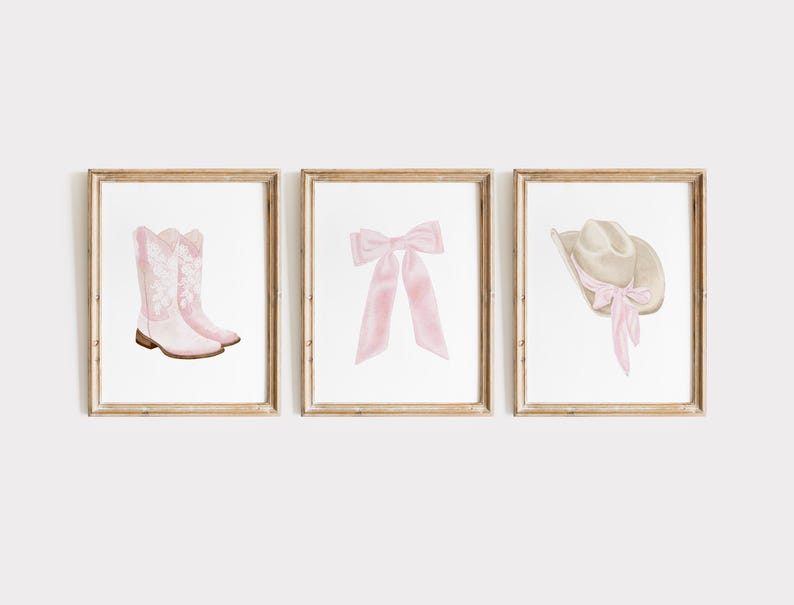 K&ouml;nnte beinhalten: Drei gerahmte Drucke mit Aquarellillustrationen. Die Drucke zeigen ein Paar rosa Cowboystiefel, eine rosa Schleife und einen Cowboyhut mit rosa Band. Die Rahmen haben eine hellbraune Holzoberfl&auml;che. Das Kunstwerk ist vor einem wei&szlig;en Hintergrund.