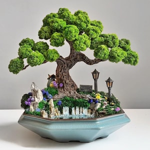 May include: A detailed miniature bonsai tree with a landscape scene. The tree features a textured brown trunk and bright green foliage. The scene includes a waterfall, miniature figures, a bench, and street lamps, set in a light blue hexagonal pot.