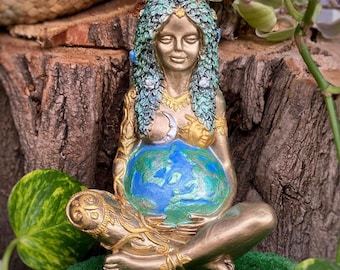 May include: A gold-toned statue of a woman holding a blue and green globe. She is wearing a crown of leaves and has a crescent moon and sun on her chest.