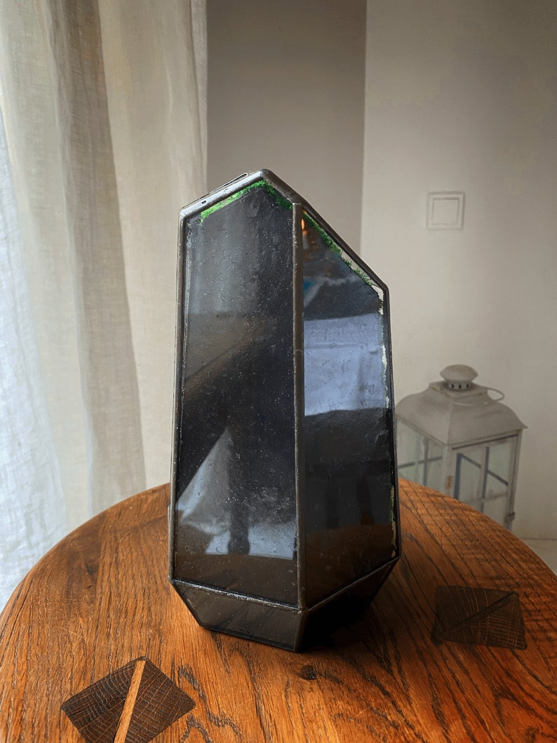 Op de afbeelding: Een zwarte geometrische glazen kaarsenhouder met een groene glazen accent. De houder staat op een houten tafel.