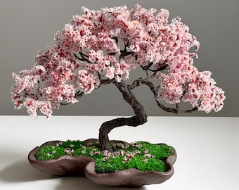 May include: A miniature bonsai tree with a dark brown, curved trunk and branches. The tree is adorned with pink and white blossoms. It sits in a brown, organic-shaped pot filled with green moss and small pink accents.