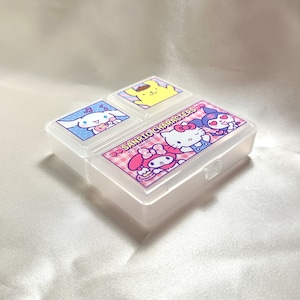 May include: A clear plastic pill box with four compartments. Each compartment features a different Sanrio character: Hello Kitty, My Melody, Little Twin Stars, and Cinnamoroll. The box has the text "SANRIO CHARACTERS" and "©'22 SANRIO Ⓡ" printed on the front.