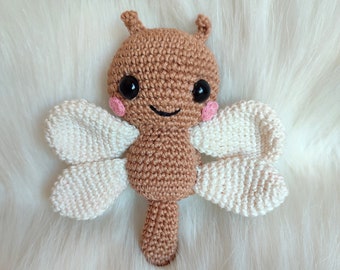 May include: A crocheted brown butterfly toy with white wings and black eyes. The butterfly has a smiling face and pink cheeks.