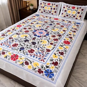 May include: White bedspread and two pillowcases with colorful floral embroidery. The design features red, yellow, blue, and purple flowers with green leaves on a white background. The bedspread has a blue border.