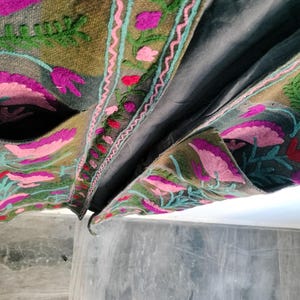 May include: Close-up of a gray embroidered jacket with a floral design. The jacket features pink, purple, and green floral embroidery on a gray background. The jacket has pockets and a dark gray lining.