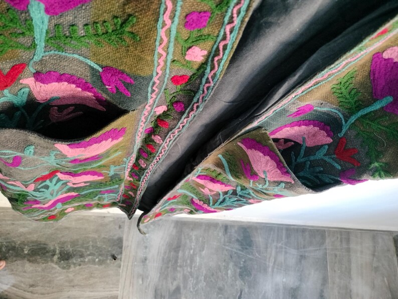 May include: Close-up of a gray embroidered jacket with a floral design. The jacket features pink, purple, and green floral embroidery on a gray background. The jacket has pockets and a dark gray lining.
