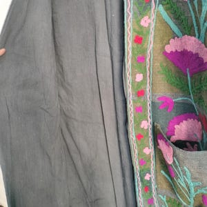 May include: A gray coat with floral embroidery. The coat features a dark gray fabric with a detailed embroidered border. The border includes pink and red flowers with green leaves and a teal outline.