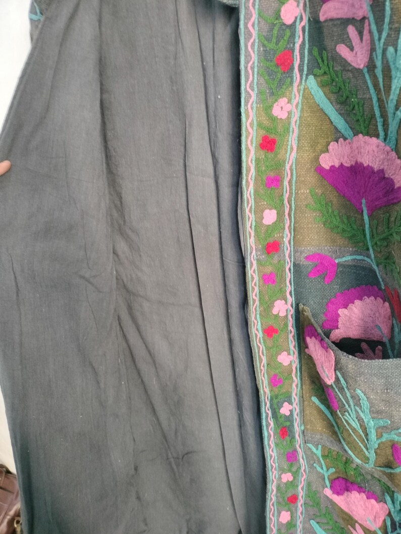 May include: A gray coat with floral embroidery. The coat features a dark gray fabric with a detailed embroidered border. The border includes pink and red flowers with green leaves and a teal outline.