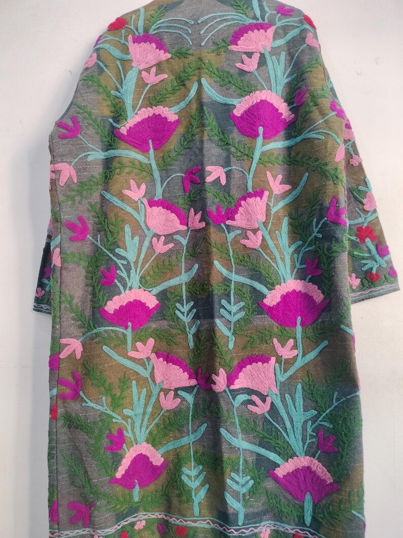 May include: A long, gray embroidered coat featuring a floral design. The coat has a pattern of large, magenta and pink flowers with teal stems and green leaves. The sleeves are three-quarter length. The coat is made of a soft, textured fabric.