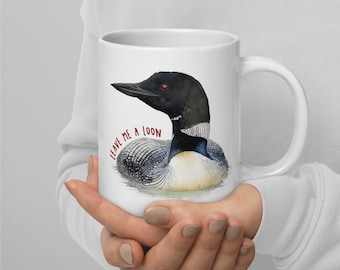 May include: White ceramic mug featuring a watercolor illustration of a loon with the text "LEAVE ME A LOON" in red. The loon has black, white, and gray feathers, a black beak, and a red eye. The mug has a white handle.