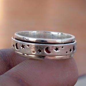 Peut inclure: Une bague rotative de couleur argentée présentant un motif découpé de croissants de lune et d'étoiles sur la bande centrale. La bague possède une finition métallique polie avec une bande extérieure distincte qui tourne indépendamment de la structure.