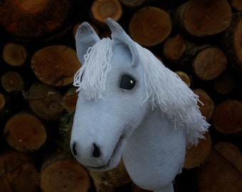 May include: A light blue stuffed horse head with a white mane and tail. The horse is posed against a background of stacked wooden logs.