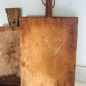 May include: Two rectangular wooden cutting boards with visible surface scratches and wear. Each board features a vertical handle at the top, with one handle including a thin, looped twine cord for hanging. The wood displays a natural brown grain.