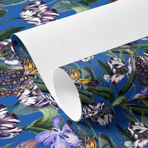 Pode incluir: Um rolo de papel de parede com um padrão floral sobre um fundo azul brilhante. O design inclui tulipas brancas e roxas, flores amarelas e laranja e folhas verdes. O papel está parcialmente desenrolado, revelando um interior branco.