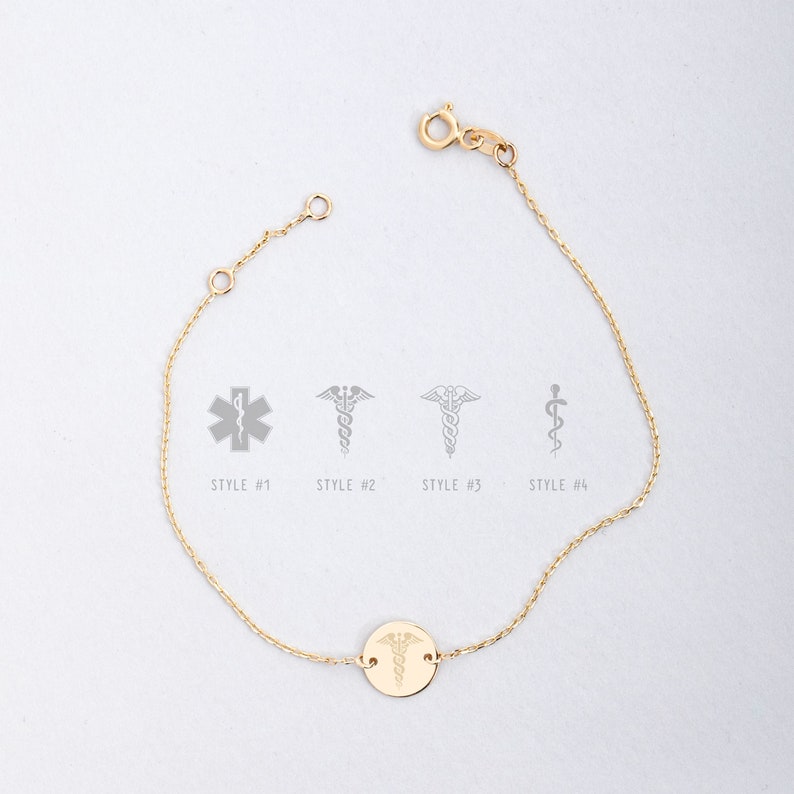 Op de afbeelding: Een gouden kettingarmband met een ronde bedel met een medisch symbool. De bedel heeft een caduceus-ontwerp met een slang die om een staf met vleugels is gewikkeld. De armband wordt getoond tegen een witte achtergrond.