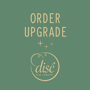 May include: A green background with the text "ORDER UPGRADE" in a light yellow color. Below the text is a stylized logo of a circle with the word "disc" in a light yellow color and the text "FINE JEWELRY" below it.