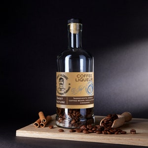 Pode incluir: Uma garrafa de vidro transparente de licor de café com rolha. O rótulo diz "Grandpa Tadeusz Craft Alcohol Coffee Liqueur Sweet Tincture". Grãos de café enchem a garrafa. Pauzinhos de canela e grãos de café numa tábua de madeira.