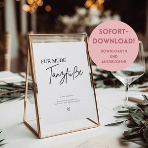 May include: A printable sign in a gold frame that reads "FÜR MÜDE Tanzfüße" with the text "Liebe Madels, Zieht Eure Schuhe aus und lasst uns weiter tanzen!" and a heart symbol. The sign is on a table with a glass of water and greenery.