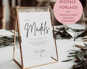 May include: A gold-framed sign with the words "Liebe Mädels" in elegant script. The sign includes additional text and a heart symbol. A pink circle in the background reads "DIGITALE VORLAGE!" and other text. The sign is on a white table.