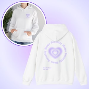 Peut inclure: Un sweat à capuche blanc avec une poche avant et une capuche. L'avant présente un petit cœur violet avec du texte. Le dos présente un grand cœur violet dans un cercle, avec les mots "Sorority Name" autour.