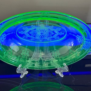 May include: A green Depression glass serving dish with an etched floral design. The dish is oval shaped and has a raised rim.