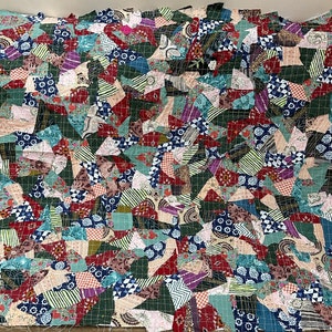 May include: A patchwork quilt made from a variety of fabrics in shades of red, green, blue and pink. The quilt is made up of many small squares and triangles, creating a complex and interesting pattern.
