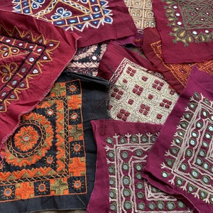 Puede incluir: Surtido de cuadrados de tela coloridos con bordados intrincados y adornos de espejo. Los cuadrados son en tonos de rojo, negro y blanco, y presentan patrones geométricos y motivos florales.