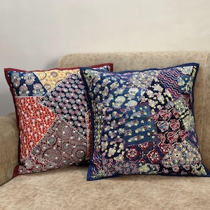 May include: Two decorative throw pillows with a patchwork design. The pillows are made of fabric with a variety of colors and patterns, including red, blue, yellow, and white. The pillows are sitting on a brown couch.