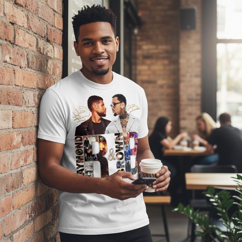May include: White t-shirt featuring a graphic design with the text "Raymond & Brown" and images of two men. The shirt is being worn by a person. The person is holding a coffee cup and a phone.