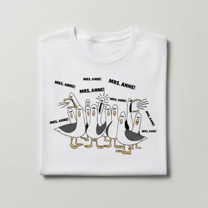 May include: White t-shirt featuring a cartoon illustration of seagulls with the text "MRS. ANNE!" in speech bubbles. The seagulls are in various poses, with black and white feathers and yellow feet.