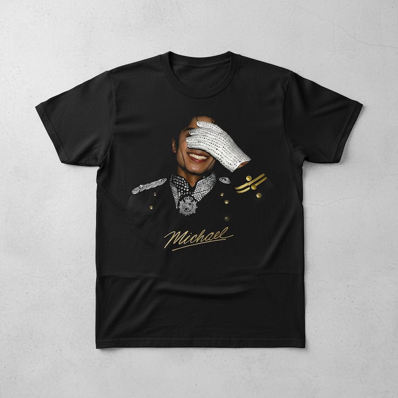 May include: Black t-shirt featuring a portrait of a smiling person wearing a military-style jacket and a white, bejeweled glove covering their eyes. The word "Michael" is written in gold script below the portrait.