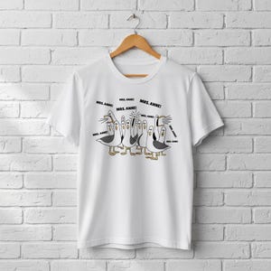 May include: White t-shirt featuring a cartoon illustration of seagulls with the text "MRS. ANNE!". The seagulls are in various poses, with black and white bodies, yellow feet, and open beaks. The shirt is hanging on a wooden hanger.