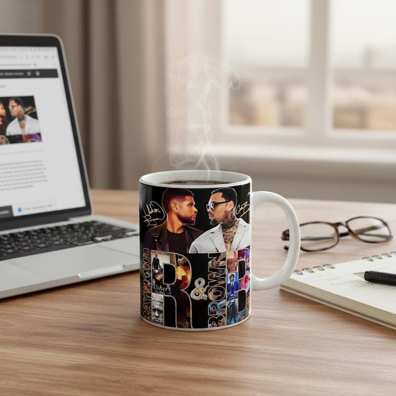 May include: A white ceramic coffee mug featuring a collage of images and text. The mug showcases two men, signatures, and the words "R & B" with the names "Usher" and "Brown". Steam rises from the mug, suggesting a hot beverage.